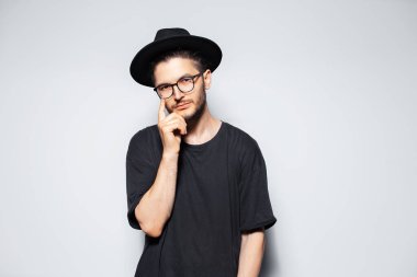 Siyah gömlek, şapka ve gözlük takan düşünceli genç adamın stüdyo portresi..