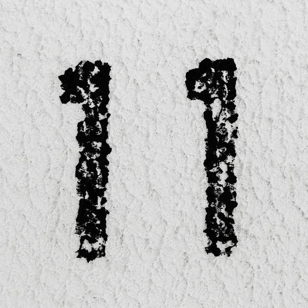 Close-up of black painted number of 11 on background of grey textured wall.