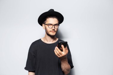 Beyaz üzerine akıllı telefon kullanan şapkalı bir adamın stüdyo portresi..