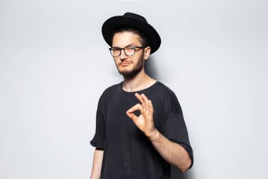 Kendine güvenen adamın stüdyo portresi, gri arka planda 'iyi' jestini gösteriyor.