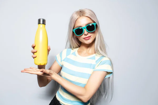 Portrait of pretty girl in striped shirt holding metal water bottle on white.