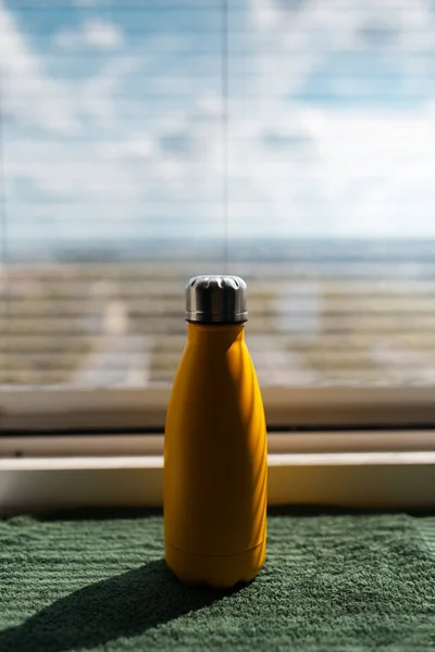 Close-up of yellow metal thermo water bottle on background of window.