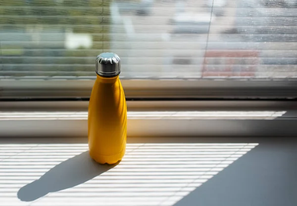 Close-up of yellow metal thermo water bottle on window sill.
