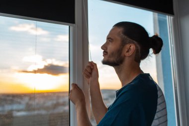 Kapalı genç adamın portresi güneşli bir günde yuvarlanmış jaluziler..