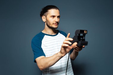 Polaroid fotoğraf makinesiyle fotoğraf çeken genç bir adamın stüdyo portresi..