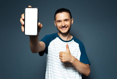 Genç mutlu bir adamın portresi, baş parmağını kaldırması, akıllı telefonu elinde tutması....