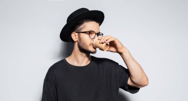 Gri arka planda kağıt bardaktan kahve içen genç hippinin stüdyo portresi..