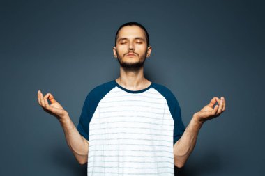 Mavinin arka planında meditasyon yapan genç bir adamın stüdyo portresi.