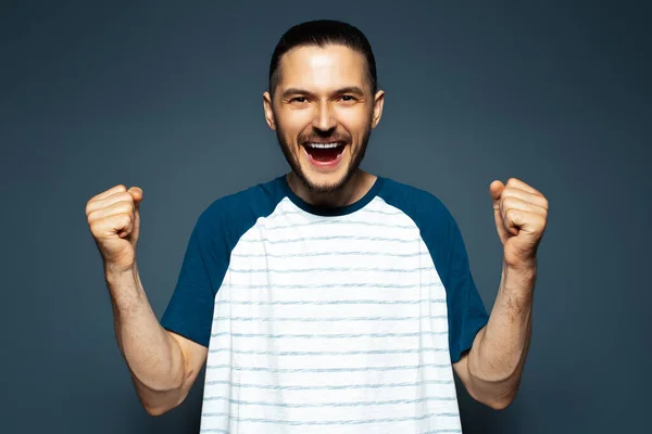 Yes. Studio portrait of young happy man rejoicing his victory. Blue background.
