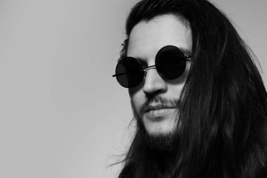 Black and white studio portrait of young serious man with long hair,  wearing round sunglasses. Copy space concept.