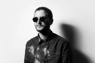 Black and white studio portrait of young handsome man with beard, wearing shades.