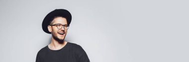 Studio portrait of young happiness man wearing eyeglasses and black hat on grey background with copy space. Panoramic banner view.