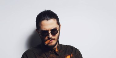Studio portrait of young man smoking a cigar, wearing round sunglasses on white background. Panoramic banner.