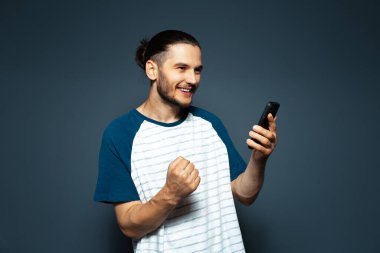 Studio portrait of young smiling confident man, holding smartphone.