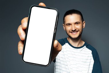 Portrait of young smiling man holding smartphone with mockup on blue background. Blank on screen.