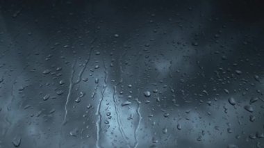 Close-up of raindrops pouring on window against blurred cloudy dark sky. Natural background.