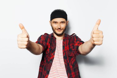 Studio portrait of young handsome man showing thumbs up on background of white, wearing red casual clothes and black head band.