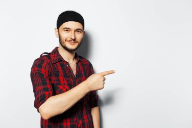 Studio portrait of young smiling guy pointing finger away on white background.