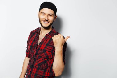 Studio portrait of young handsome smiling guy pointing finger away on white background.