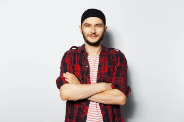 Studio portrait of young attractive guy with crossed arms, wearing red plaid shirt and black headband.