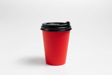Close-up of paper cup with black plastic lid for coffee takeaway of red color isolated on white studio background.