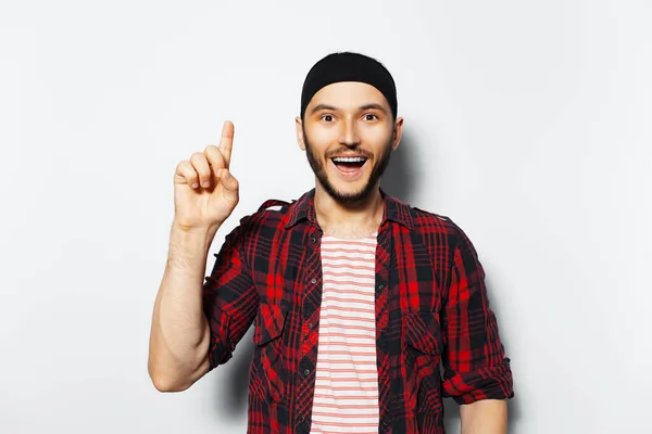Studio portrait of young happiness guy pointing index finger up, having new idea, on white background, wearing red casual clothes and black head band.