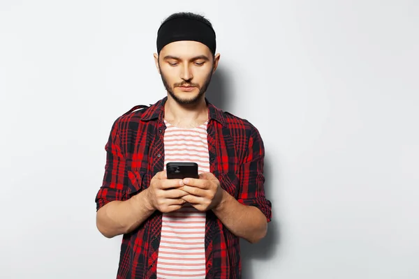Studio portrait of young man texting message on smartphone, on white background. Wearing striped shirt and plaid t-shirt.