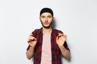 Portrait of young attractive man gesturing, wearing red plaid shirt and black headband.