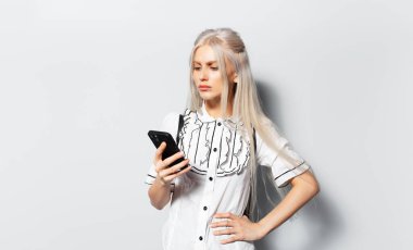 Studio portrait of young blonde pretty girl looking in smartphone on white background.