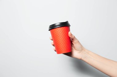 Close-up of female hand holding paper cup of red color for coffee takeaway on light grey background.
