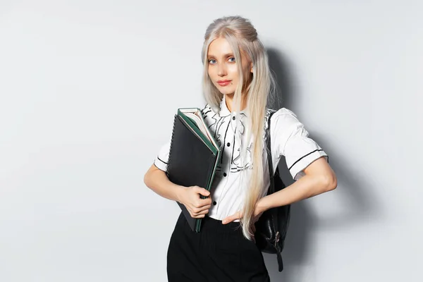 Studio portrait of young blonde beautiful girl holding a folders in hand, with backpack, on white background.