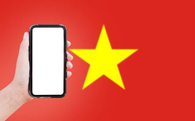 Close-up of male hand holding smartphone with blank on screen, on background of blurred flag of Vietnam.