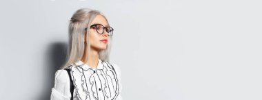 Studio portrait of young blonde pretty girl on white background, wearing eyeglasses, looking away, panoramic banner with copy space.