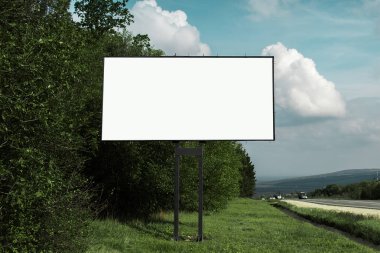Asfaltlanan yol ve yeşil ormanın yakınındaki reklam afişi için boş ilan panosu, mavi gökyüzünün arka planı..