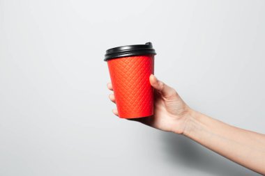 Close-up of male hand holding a paper cup for coffee takeaway of red color on white background.