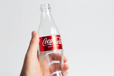 Close-up of male hand holding a empty glass bottle of Coca Cola on white background. Moldova, Chisinau - 10 august 2022.