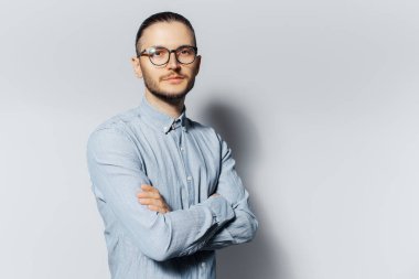 Studio portrait of young man with crossed arms, wearing eyeglasses and blue t-shirt on white background.