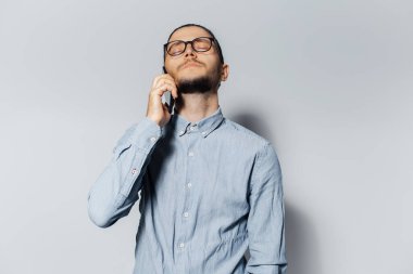 Akıllı telefondan konuşan, beyaz arka planda gözleri kapalı genç üzgün adamın stüdyo portresi..