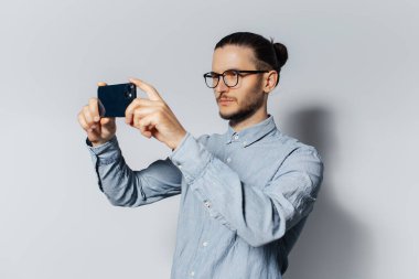 Stüdyo portresi, beyaz arka planda akıllı telefondan fotoğraf çeken ciddi bir genç..