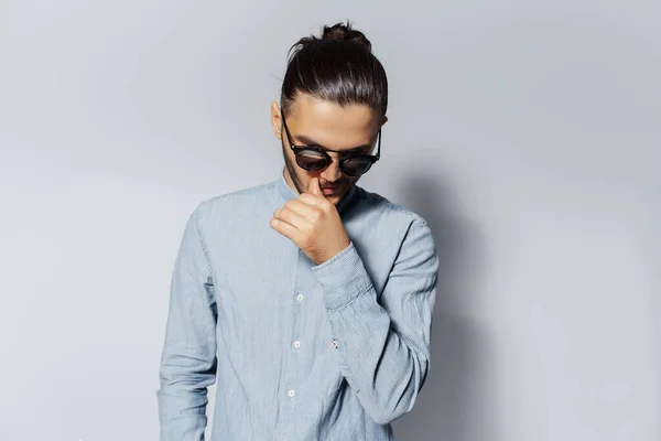 Studio portrait of young man with hair bun wearing sunglasses on white background.