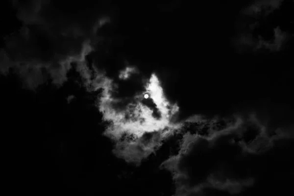 Black and white photo moon behind the clouds.
