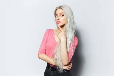 Beyaz arka planda pembe tişörtlü, sarı saçlı, gülümseyen bir kızın stüdyo portresi..