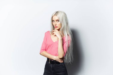 Beyaz arka planda pembe gömlekli, sarı saçlı güzel bir kızın stüdyo portresi..