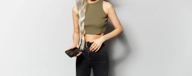 Açık gri arka planda akıllı telefonu elinde tutan sarışın kızın panoramik afişi..