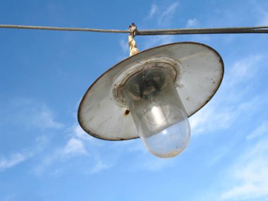An old vintage lantern hanging on a wire with light bulb - sky background