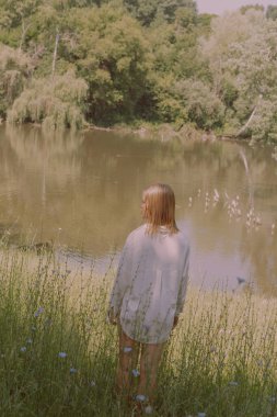 Uzun sarı saçlı güzel bir kadın nehirde yürüyor.