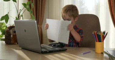 Bilgisayar kullanarak Çocuk Çalışmaları Çevrimiçi Ders Video Konferansı Sohbeti. Evde Çocuk Mesafesi Öğrenme. Anaokulu çocuğu 4K no 'lu odanın yanındaki masada oturuyor.