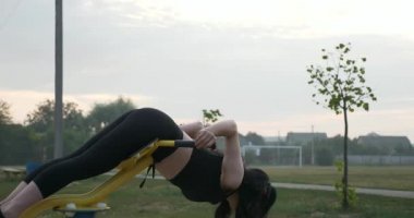 Çocuk parkında ağırlık çalıştırma antrenmanı yapan genç bir kadın. Kırsal Futbol Sahasında Güzel Kadın Vücut Çalışması. Futbol Sahası. Yaz sabahı 4K