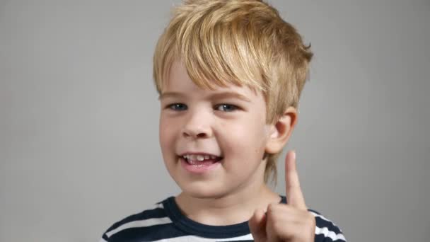 指数の指をジェスチャーを上に指す 幸せな子供の感情 ポートレートかわいい男の子 笑顔が嬉しい 白い壁の背景に対する喜びの子供 2倍スローモーション60Fps — ストック動画