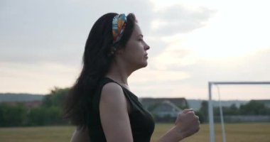 Güzel genç kadın sabah egzersizi yaparak koşuyor. Güzel Kız Formda Kadın Sporcu. Kenar mahallelerde futbol sahası var. Yaz Günü 4K